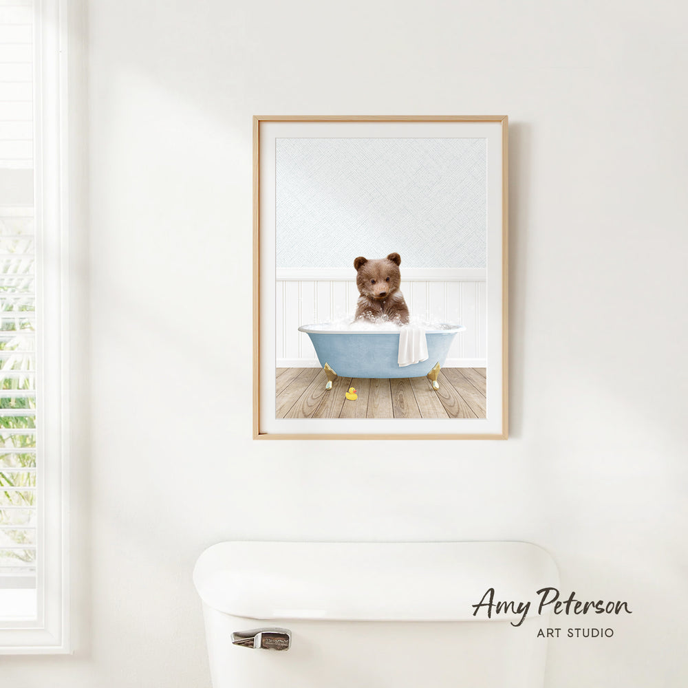 A framed image of a brown bear sitting in a blue bathtub, with a towel draped over the side of the tub.