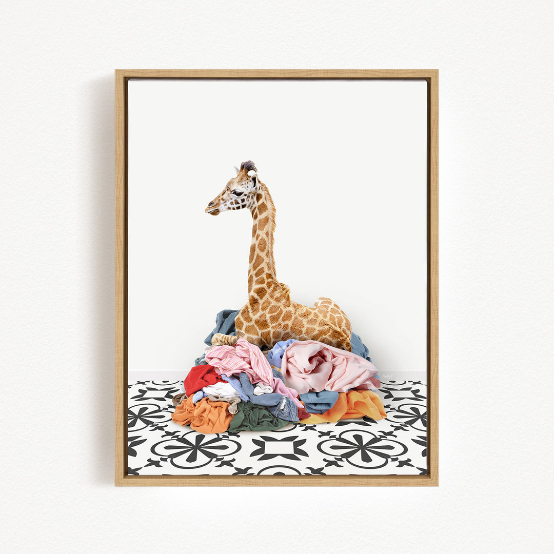 A giraffe is sitting on a pile of clothes, which are scattered on a patterned floor.