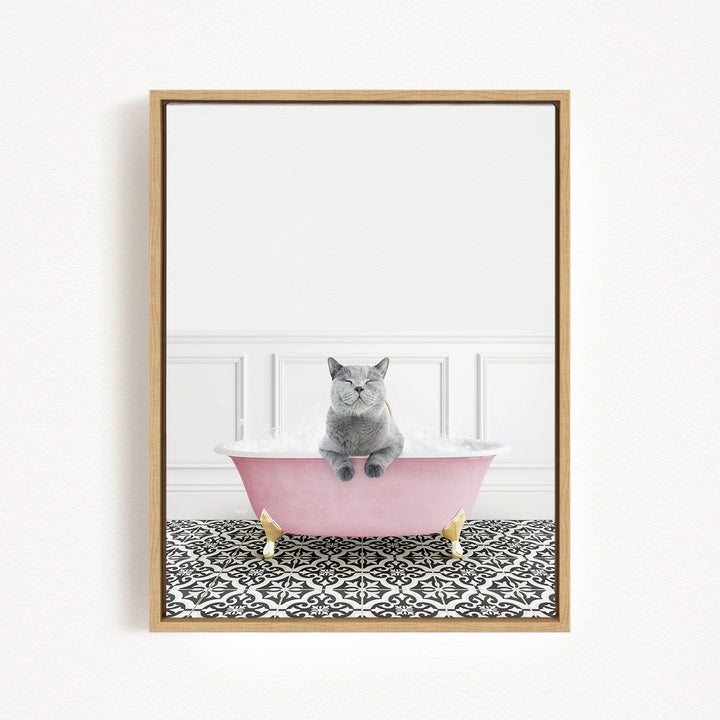 A gray cat sitting in a pink bathtub filled with bubbles, with a black and white patterned floor beneath it.