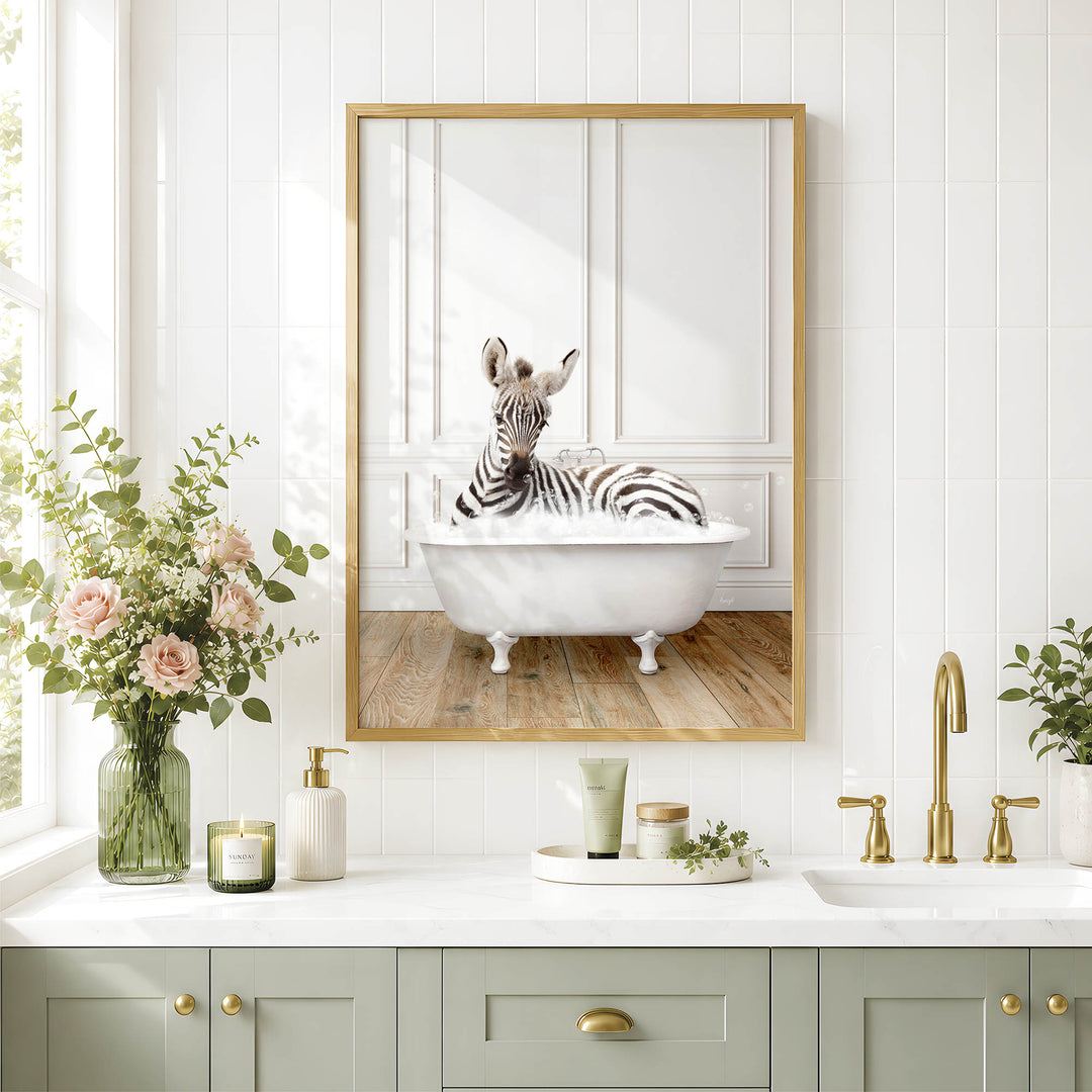 A zebra is sitting in a white bathtub in a bathroom, as depicted in a framed image on the wall above a white countertop with various toiletries and a vase of flowers.