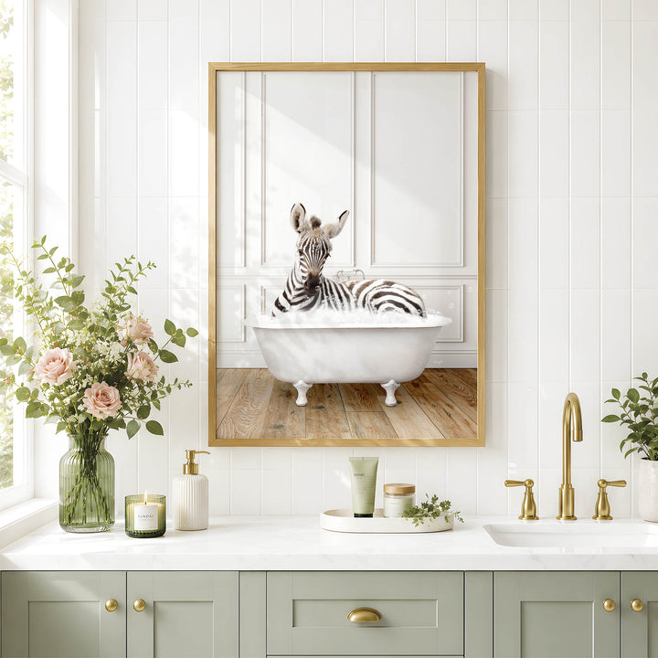 A zebra is sitting in a white bathtub in a bathroom, as depicted in a framed image on the wall above a white countertop with various toiletries and a vase of flowers.
