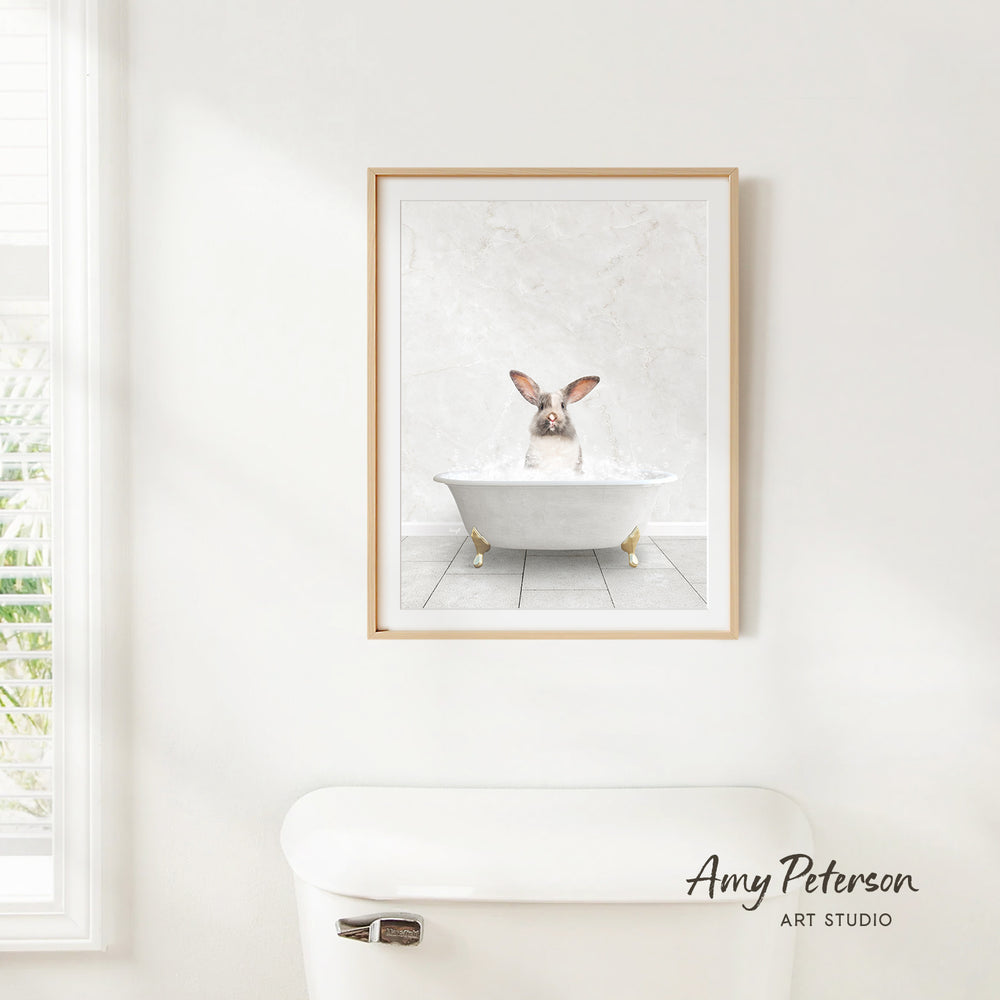 A framed print of a rabbit sitting in a bathtub is hanging on a white wall above a white toilet.