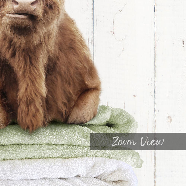A close-up of a brown animal, possibly a dog or a cat, sitting on top of a stack of towels against a white wooden background.