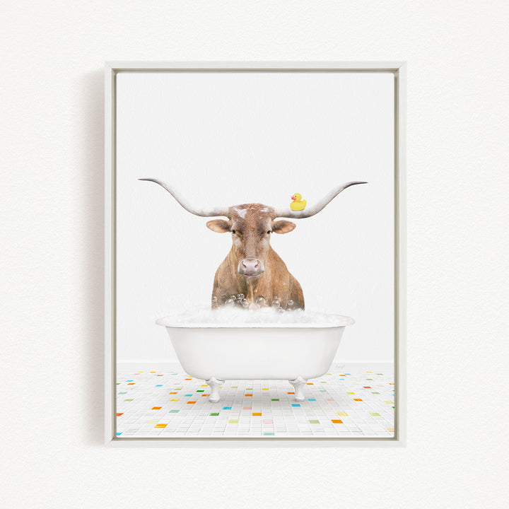 A brown cow with large horns is sitting in a white bathtub filled with bubbles, with a yellow rubber duck floating on the water.