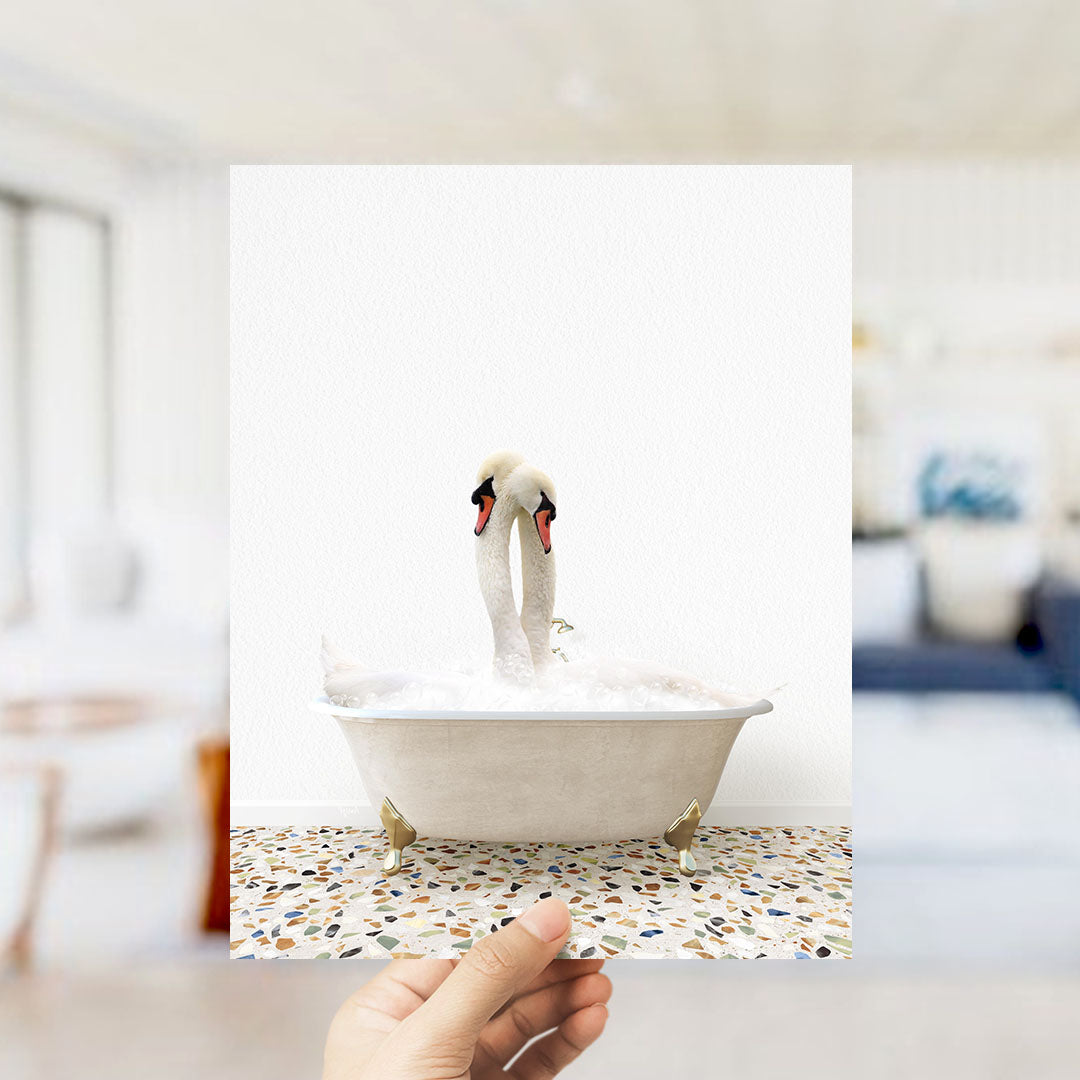 A hand holds up a photograph of two swans in a bathtub, with a blurred background suggesting a bathroom setting.