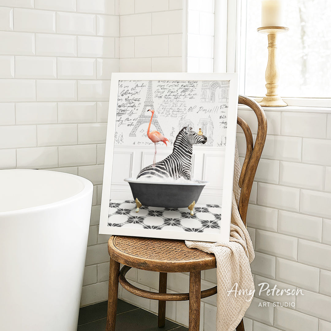 A framed image of a zebra sitting in a bathtub, with a pink flamingo standing nearby, is displayed on a wooden chair in a bathroom setting.