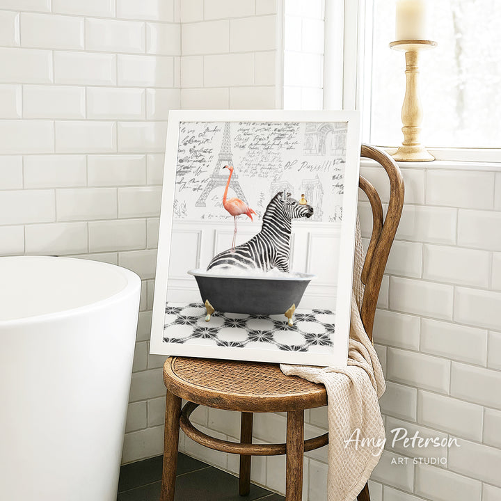 A framed image of a zebra sitting in a bathtub, with a pink flamingo standing nearby, is displayed on a wooden chair in a bathroom setting.