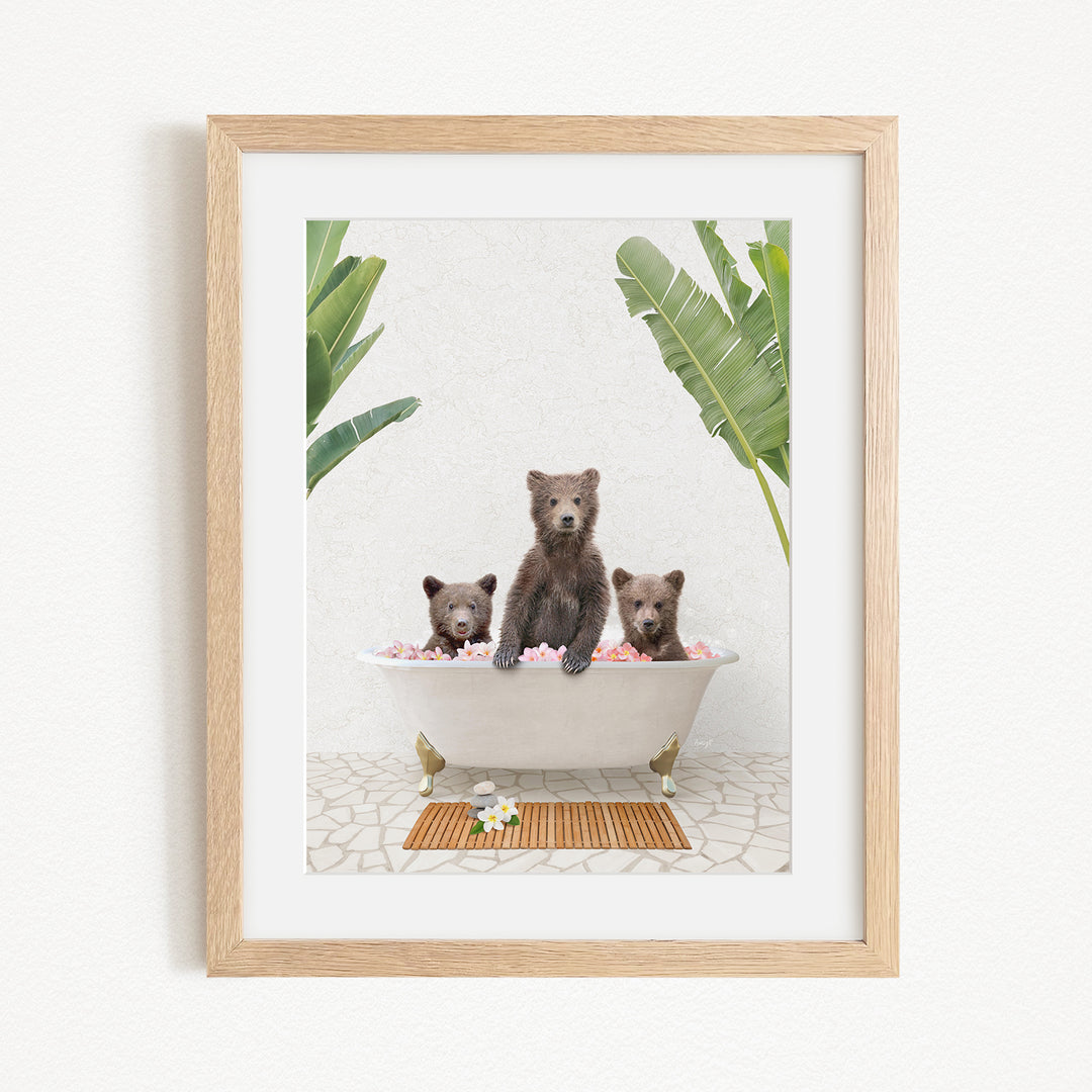 A framed image depicting three bears sitting in a bathtub filled with pink flowers, surrounded by green plants.