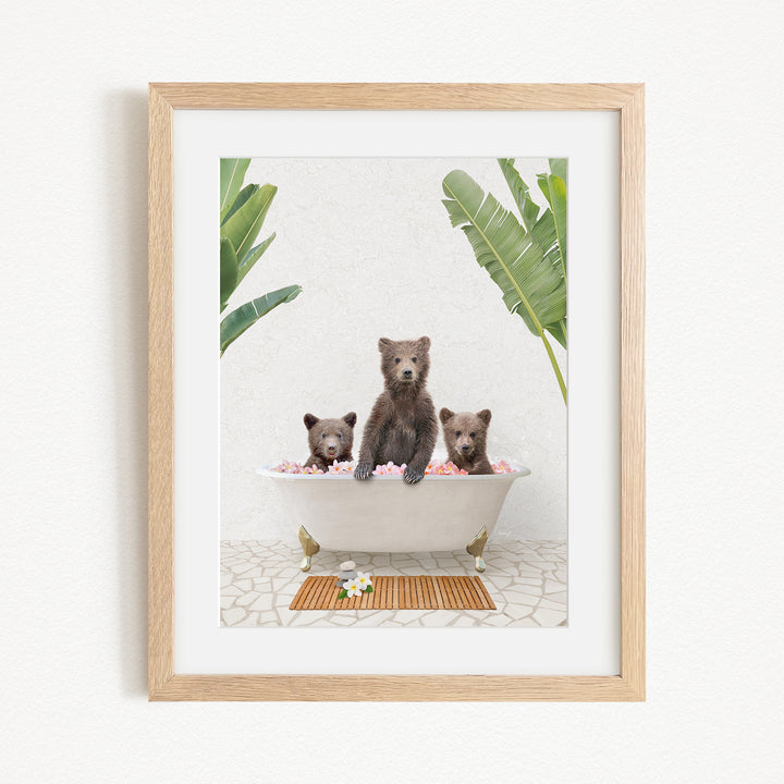 A framed image depicting three bears sitting in a bathtub filled with pink flowers, surrounded by green plants.