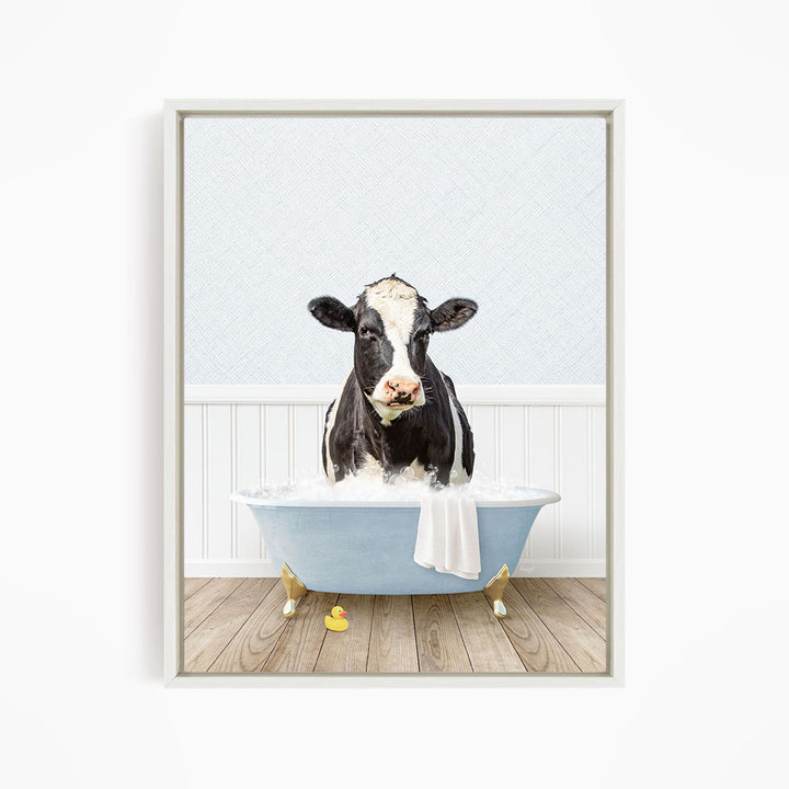 A black and white cow is sitting in a blue bathtub filled with water, surrounded by rubber duckies.