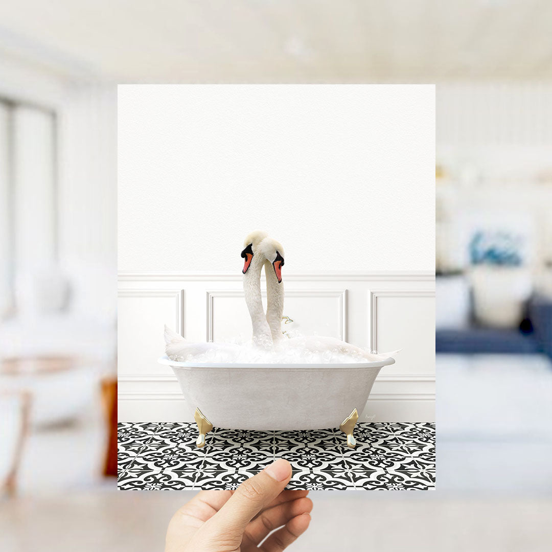 A hand holds up a framed photograph of a white swan standing in a bathtub filled with bubbles, with a blurred background suggesting a bathroom setting.