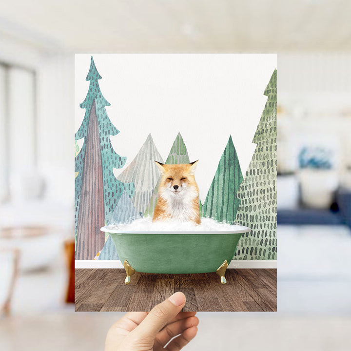 A hand holds up a framed image depicting a fox sitting in a green bathtub, surrounded by stylized trees.