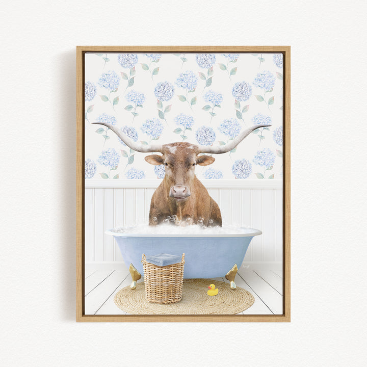 A brown steer with large horns is sitting in a blue bathtub filled with bubbles, surrounded by a wicker basket and rubber ducks.
