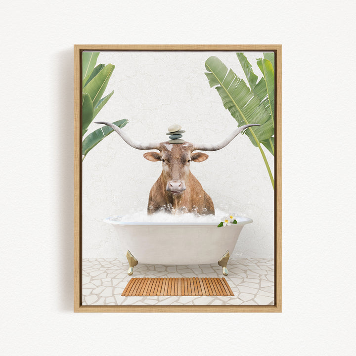 A brown cow with large horns is sitting in a white bathtub filled with bubbles, surrounded by green leaves and a wooden mat on the floor.