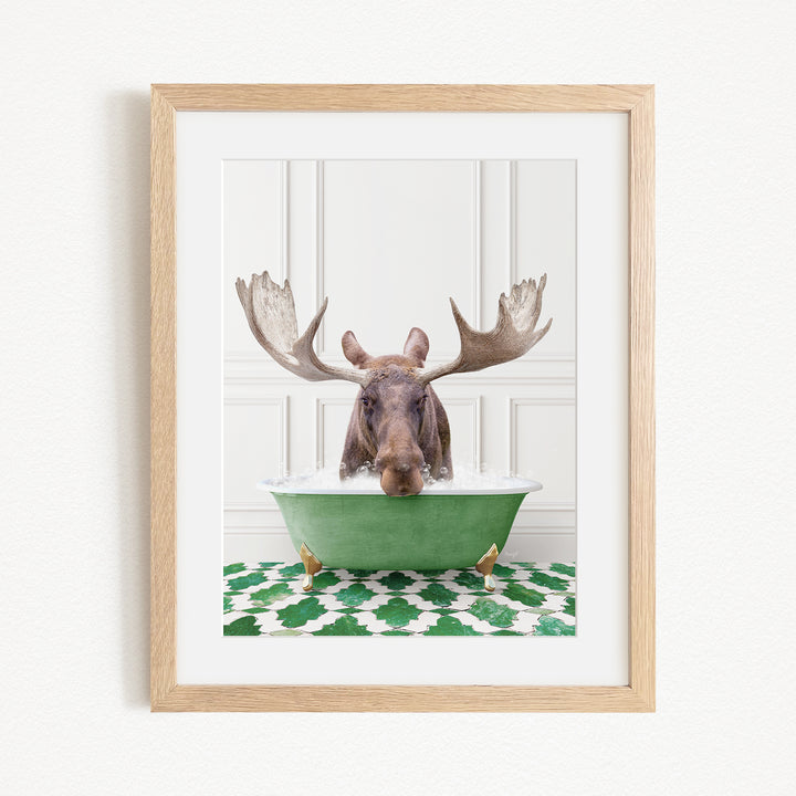 A moose with large antlers is sitting in a green bathtub, surrounded by a patterned green and white rug.