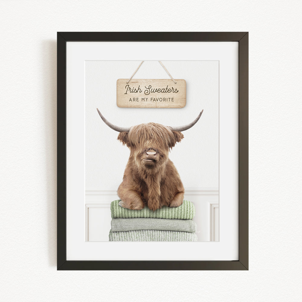 A framed image of a brown, shaggy-haired animal, likely a yak or a similar type of livestock, sitting on a stack of green blankets and wearing a sign that says "Irish Sweaters are my favorite".
