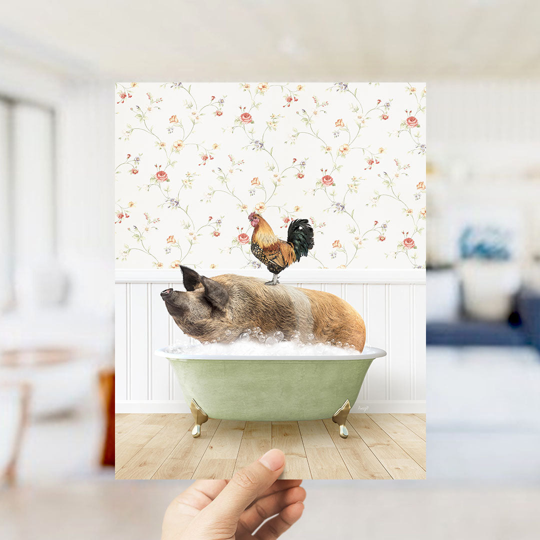 A hand holds up a framed image depicting a pig sitting in a bathtub, with a rooster perched on its back.