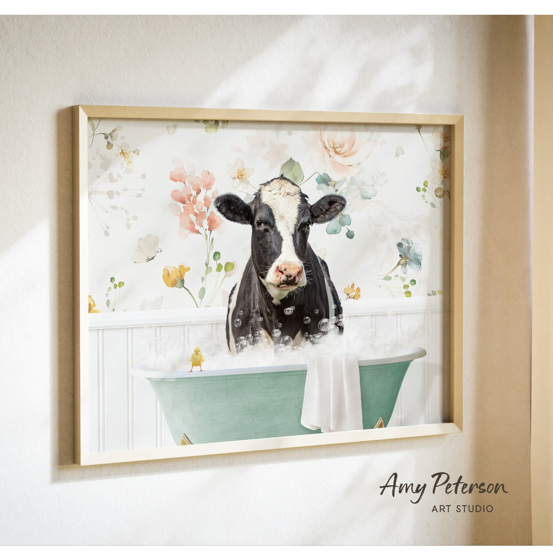 A framed print of a black and white cow sitting in a green bathtub filled with bubbles, surrounded by a floral pattern.