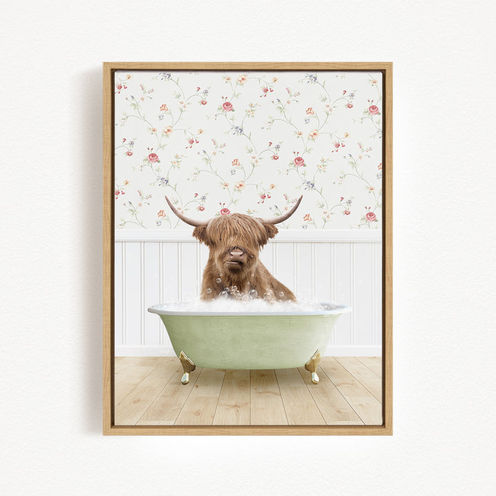 A brown cow with long horns is sitting in a green bathtub filled with bubbles, against a floral wallpaper background.