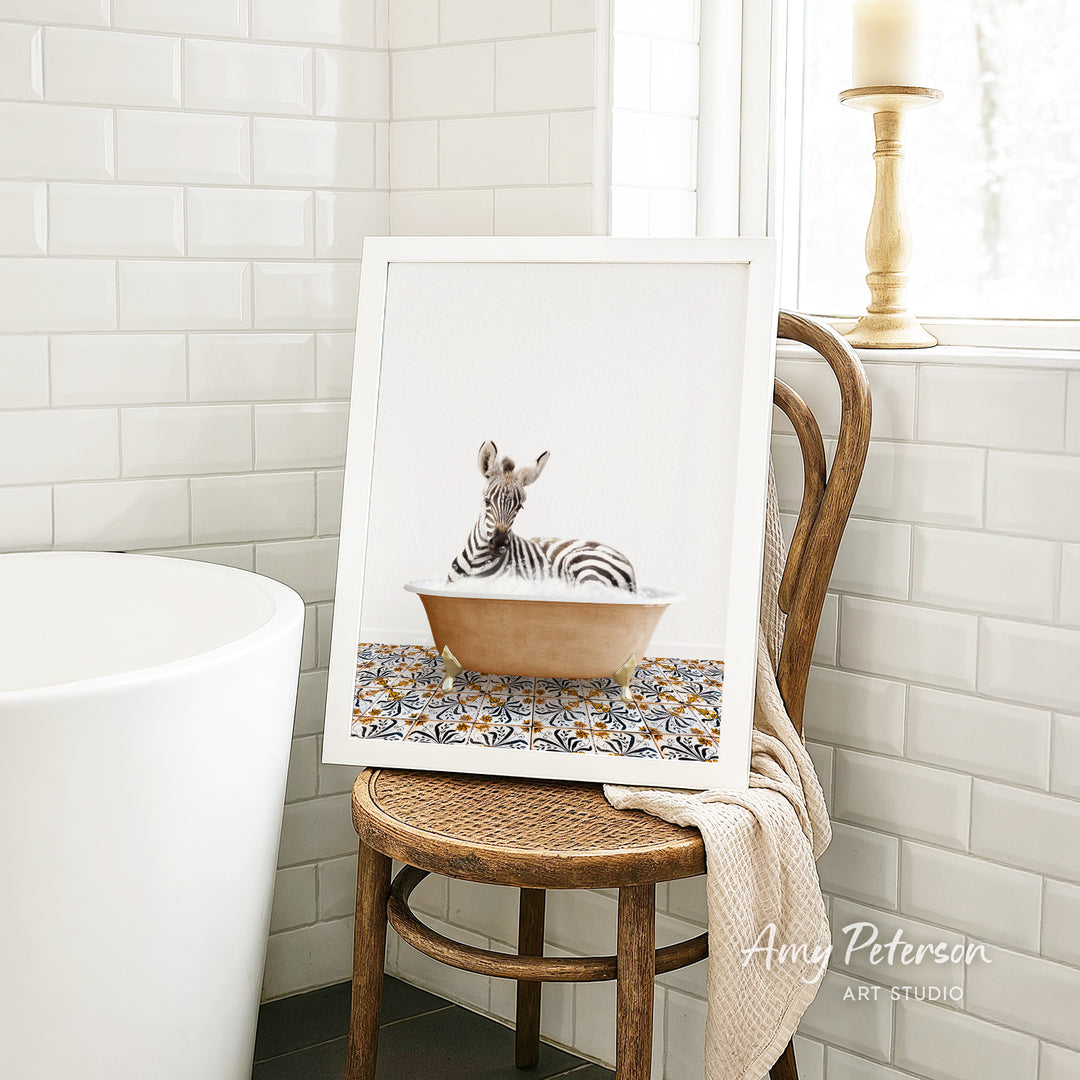 A framed image of a zebra sitting in a bathtub is displayed on a wooden chair in a bathroom setting.