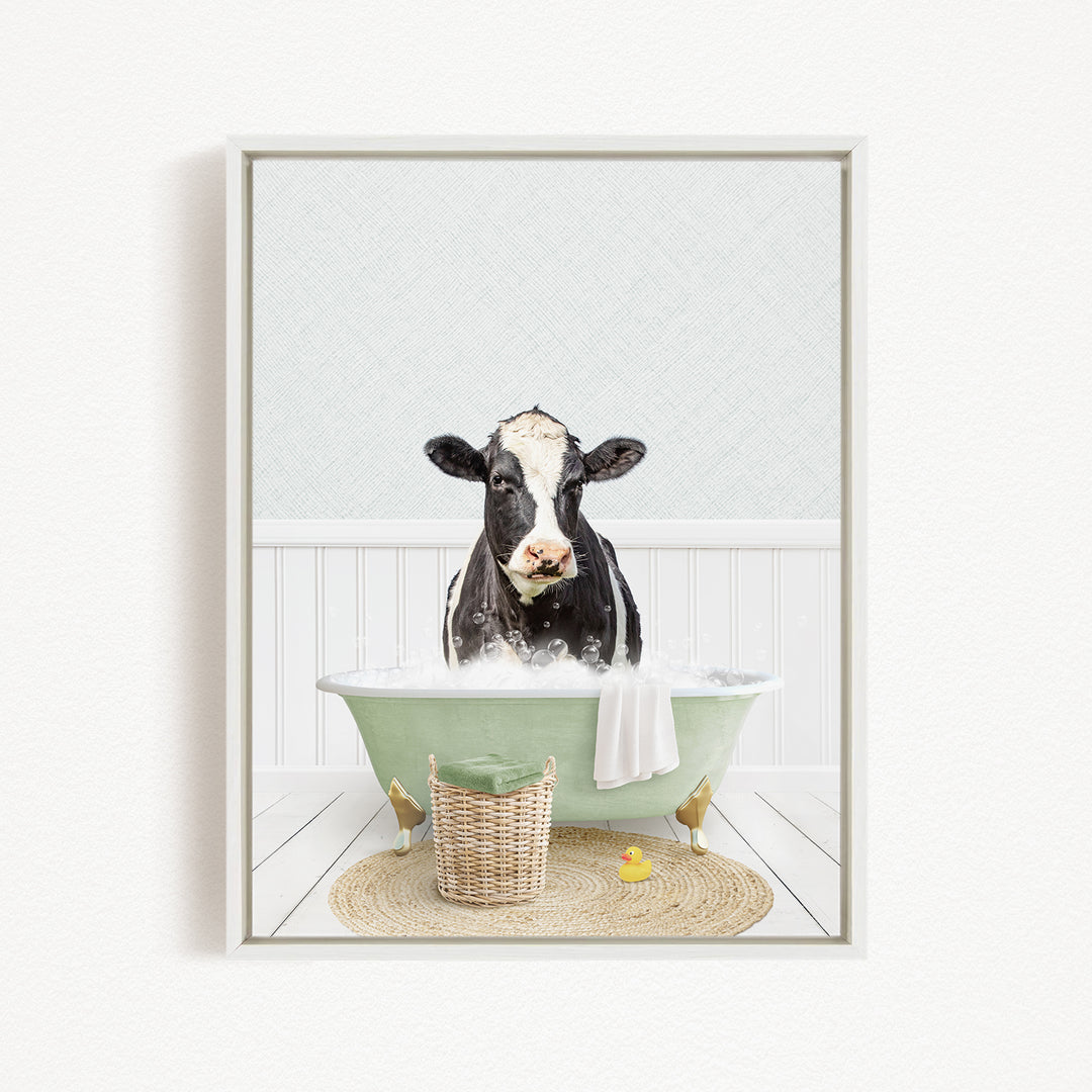 A black and white cow is sitting in a green bathtub filled with water, surrounded by a basket, a rubber duck, and a towel.