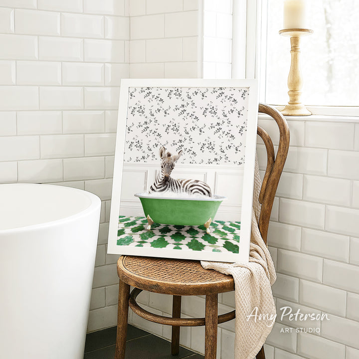 A framed image of a zebra sitting in a green bathtub is displayed on a wooden chair in a bathroom setting.