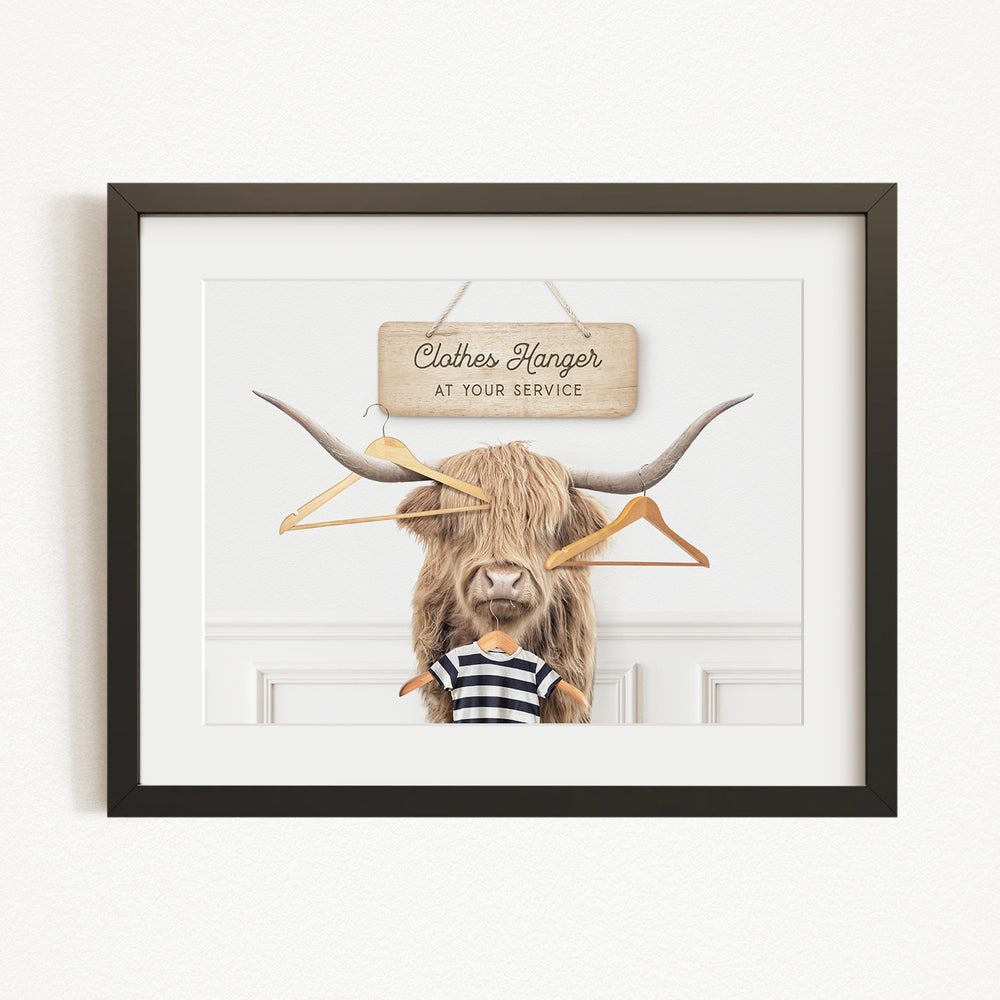 A framed image depicting a large, furry animal with a sign that reads "Clothes Hanger at your service" hanging above it.