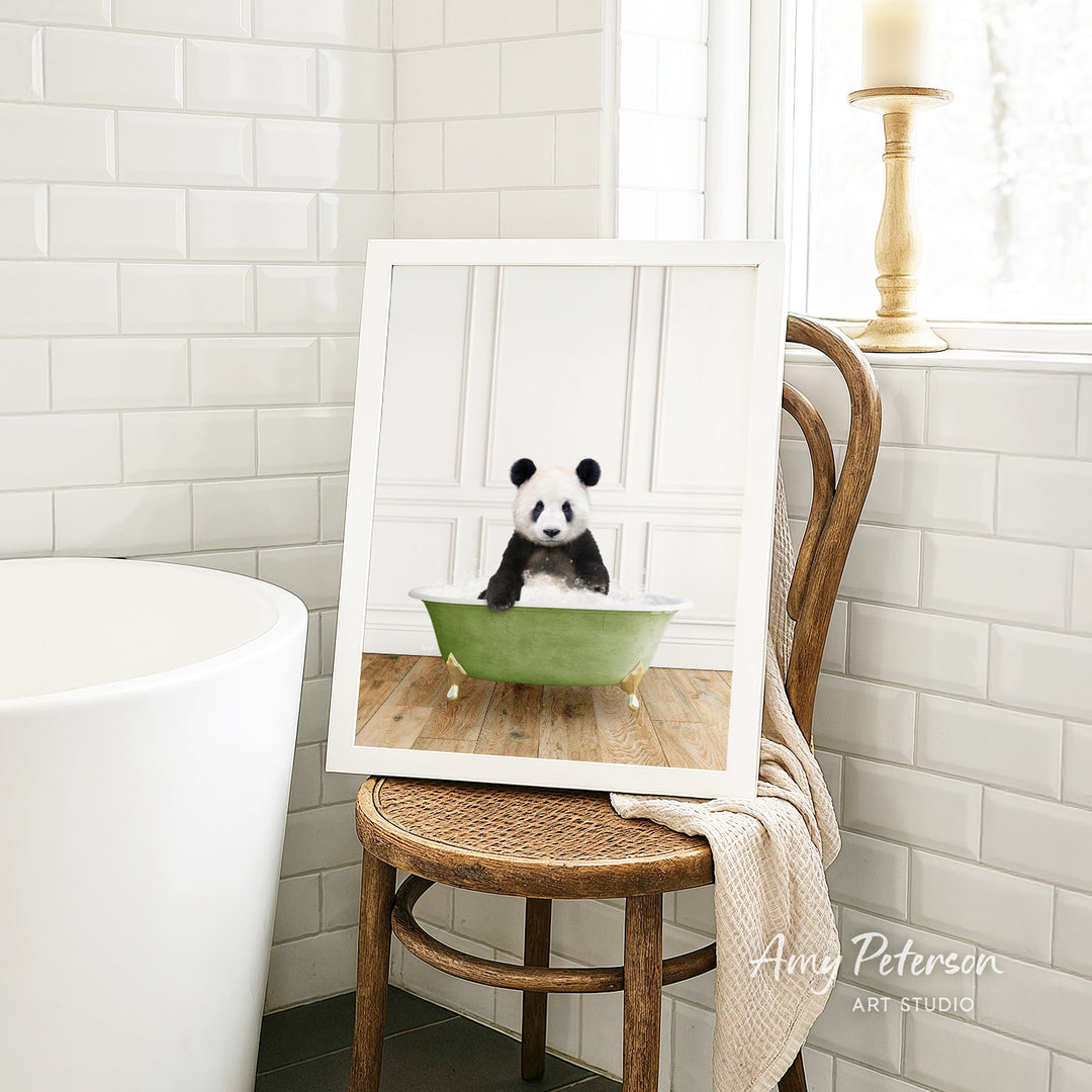 A framed image of a panda bear sitting in a green bathtub is displayed on a wooden chair in a bathroom setting.