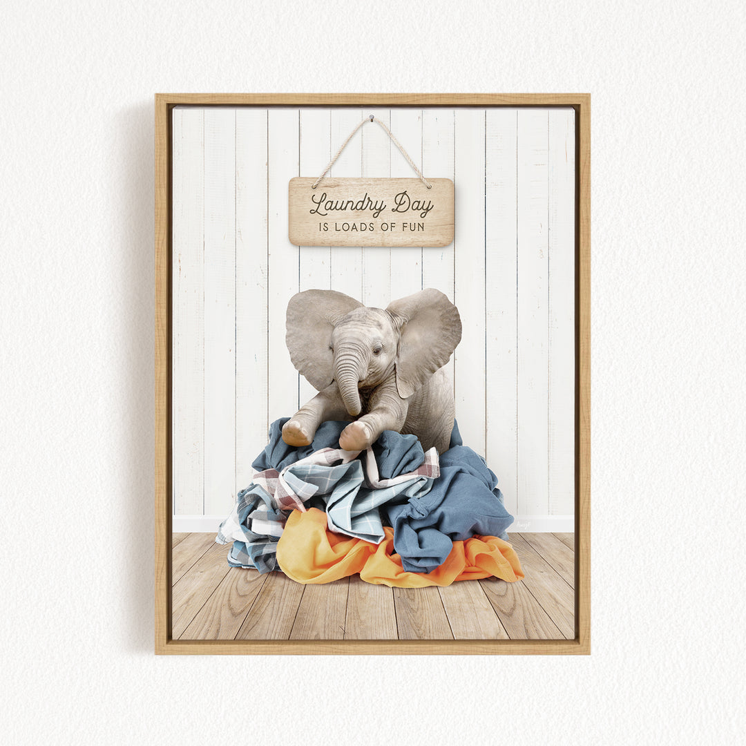 A framed image of a stuffed elephant sitting on a pile of clothes, with a sign above that says "Laundry Day is loads of fun".