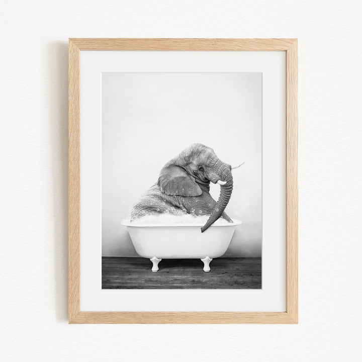 A black and white photograph of an elephant sitting in a bathtub, with its trunk raised and appearing to be enjoying the bath.