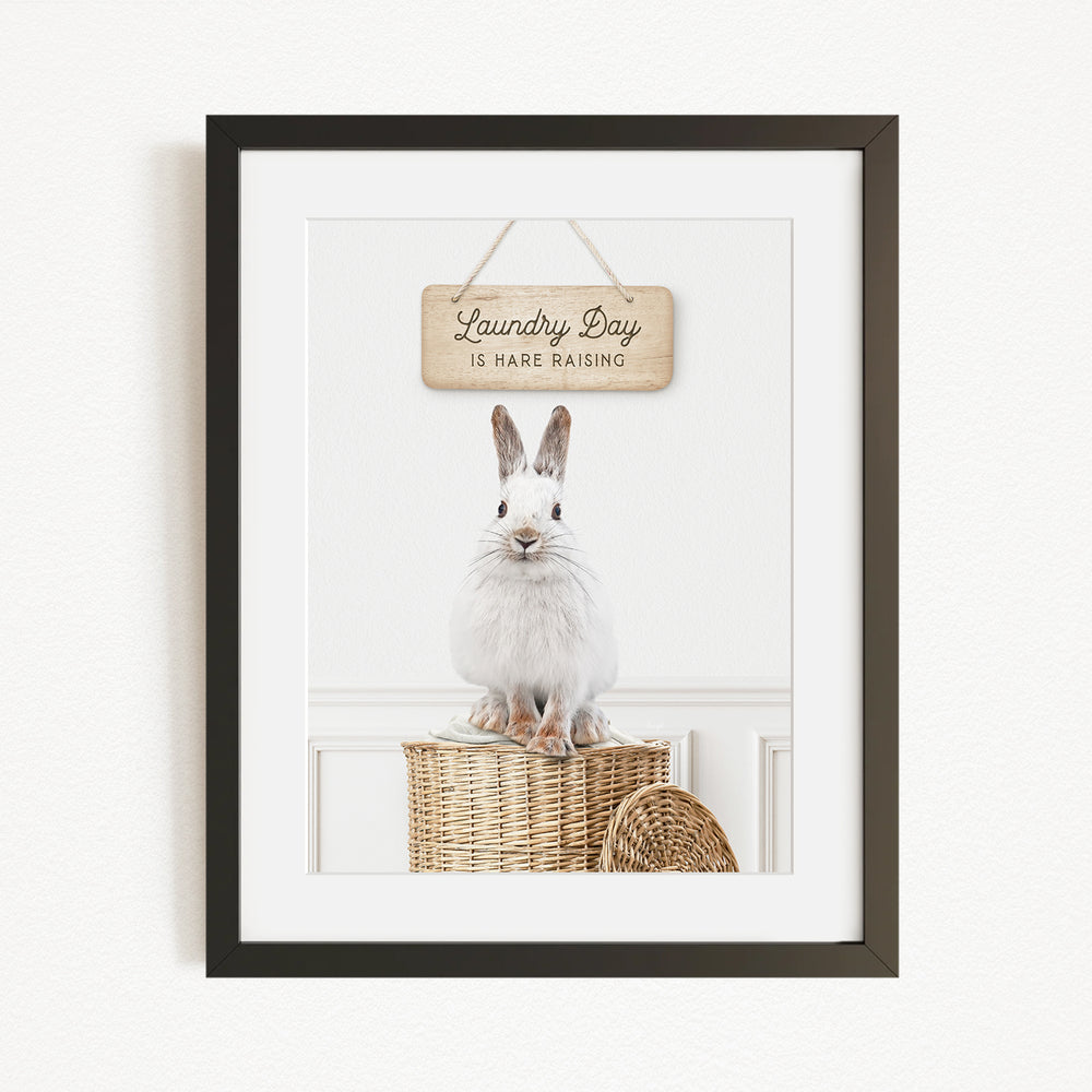 A framed image of a white rabbit sitting on a woven basket, with a wooden sign above it that says "Laundry Day is here raising".