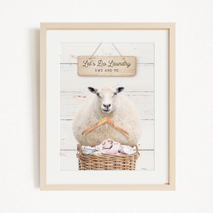 A framed image of a sheep sitting in a basket filled with laundry, with a sign above it that says "Let's Do Laundry Ew and Me".
