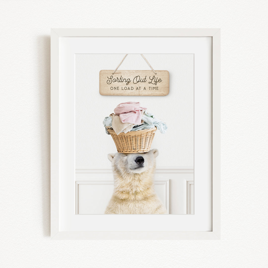 A white polar bear balancing a basket of laundry on its head, with a sign above that reads "Sorting Out Life One Load at a Time".