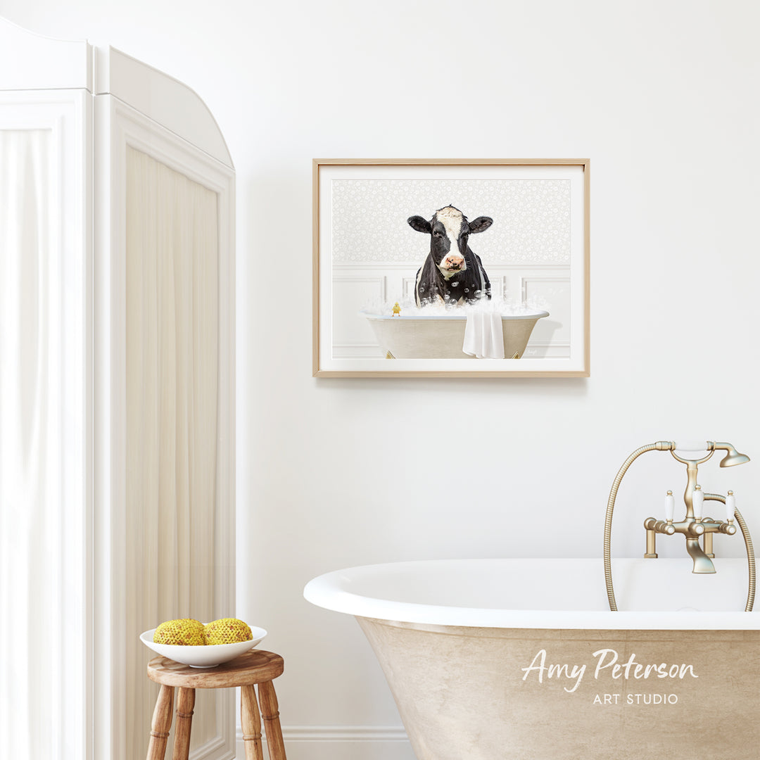 a bathroom with a framed picture of a cow sitting in a bathtub, a wooden stool, and a bowl of fruit.