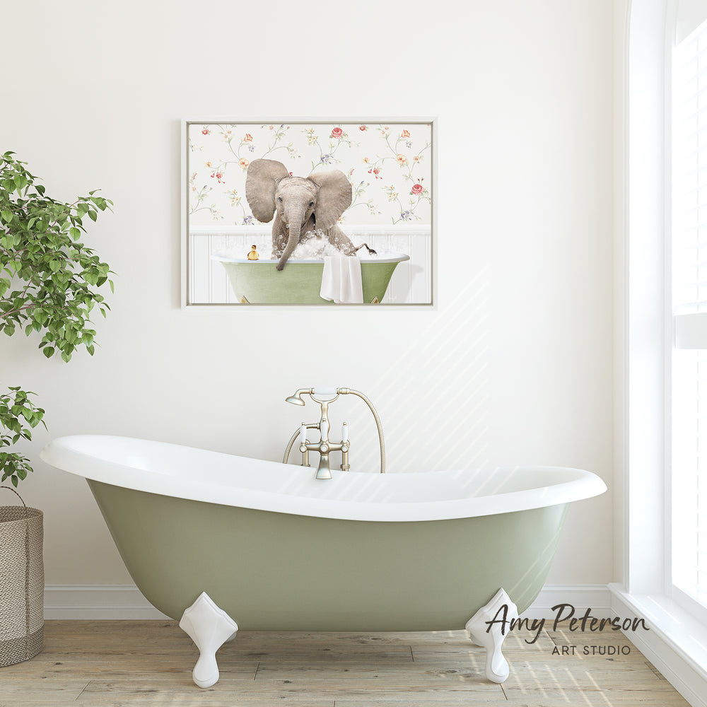 A green clawfoot bathtub with a framed image of an elephant sitting in it, set against a white wall with a floral pattern.