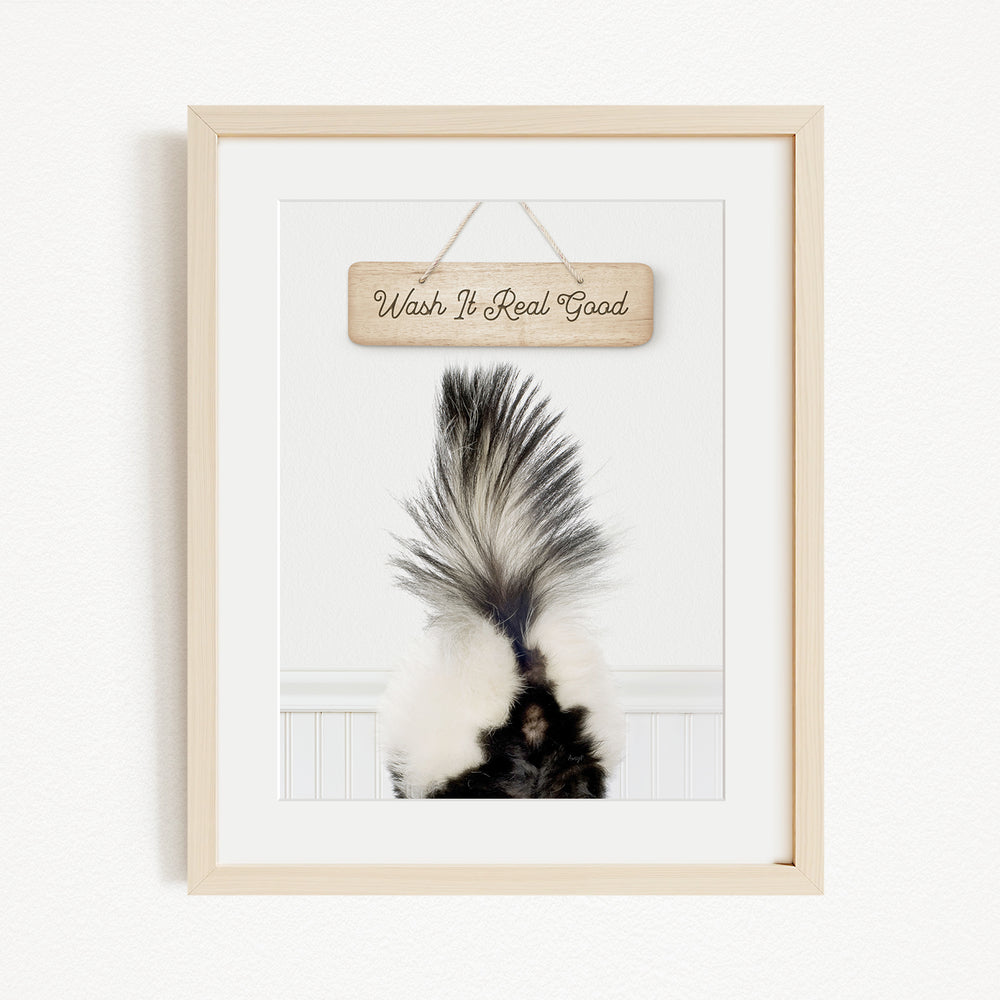 A framed image of a skunk's tail with the text "Wash it Real Good" written on a wooden sign above it.