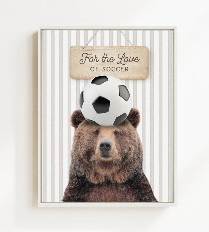 A brown bear with a soccer ball on its head, with a wooden sign above that says "For the Love of Soccer".