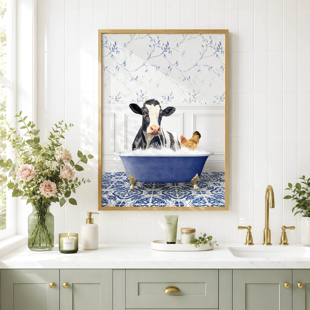 A framed image of a cow sitting in a bathtub, surrounded by flowers, is displayed on a wall above a bathroom counter with various toiletries and a vase of flowers.
