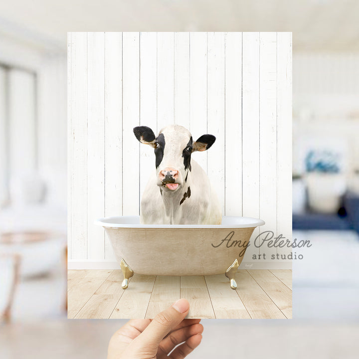 a hand holding a photo of a cow in a bathtub