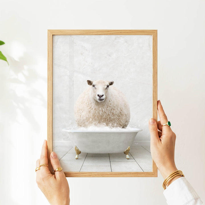 A person's hands are holding a framed picture of a sheep sitting in a bathtub filled with water.