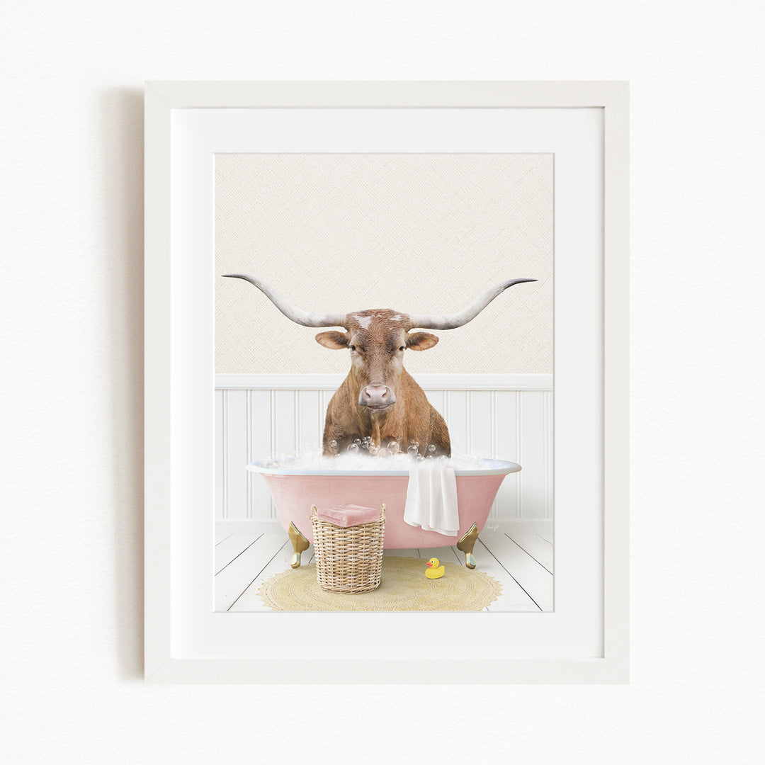 A brown cow with large horns is sitting in a pink bathtub filled with water, surrounded by a yellow rubber duck and a basket.