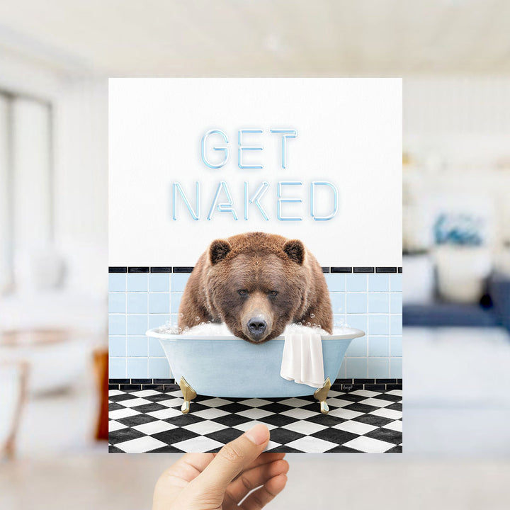 A hand holding a printed image of a brown bear sitting in a bathtub with the text "GET NAKED" displayed above it.