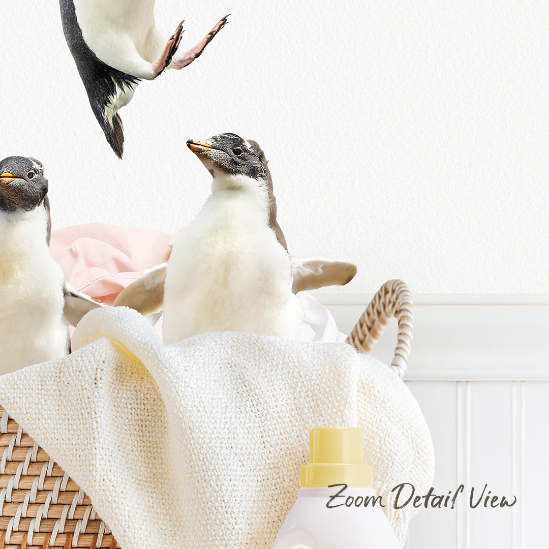 A group of penguins standing on a white towel in a basket, with a bottle of detergent visible in the foreground.