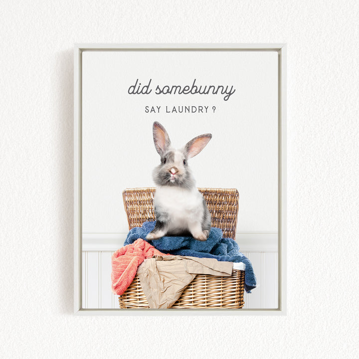 A gray and white rabbit sitting in a wicker basket filled with laundry, with the text "Did some bunny Say Laundry?" displayed above the image.
