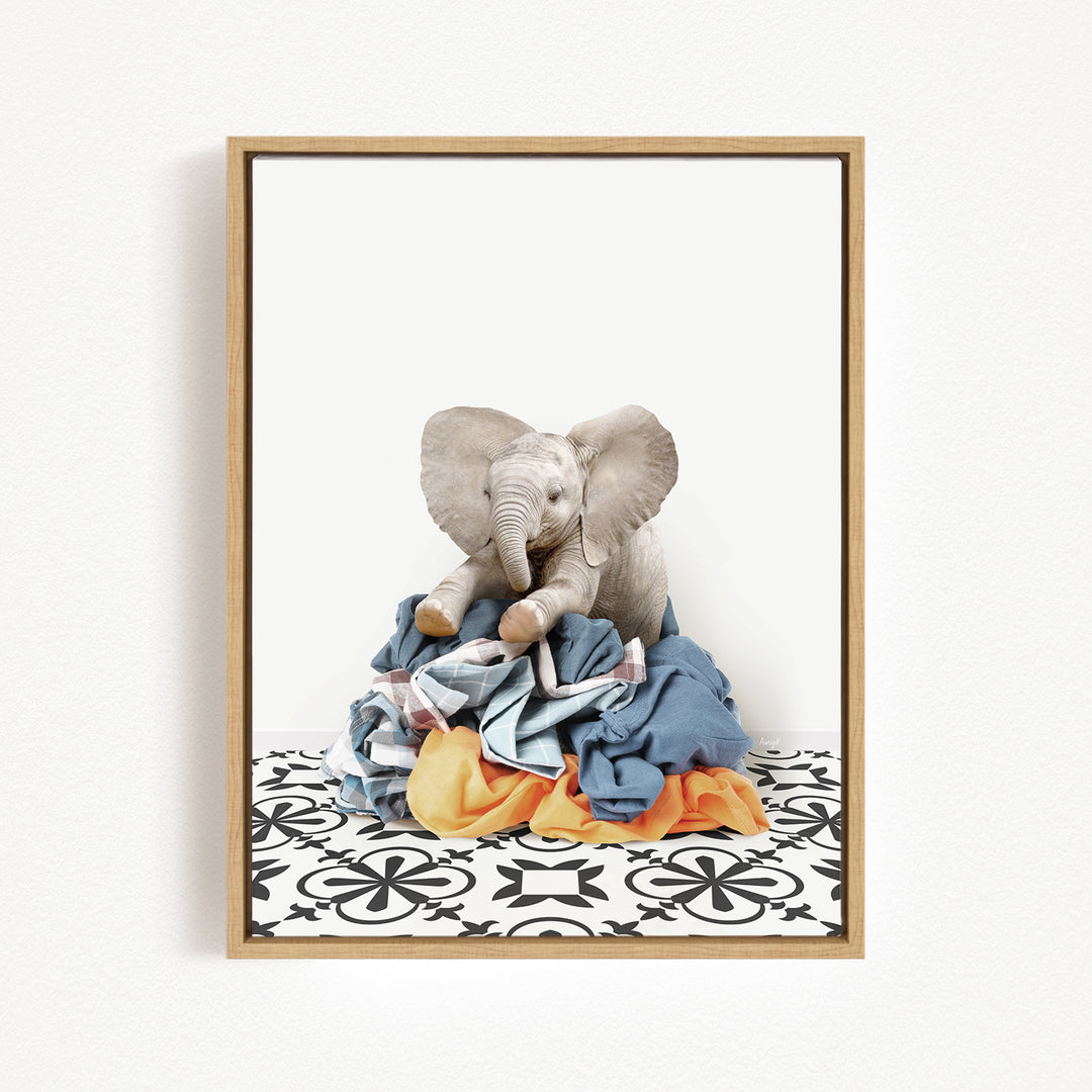 A framed image of a stuffed elephant sitting on a pile of clothes.
