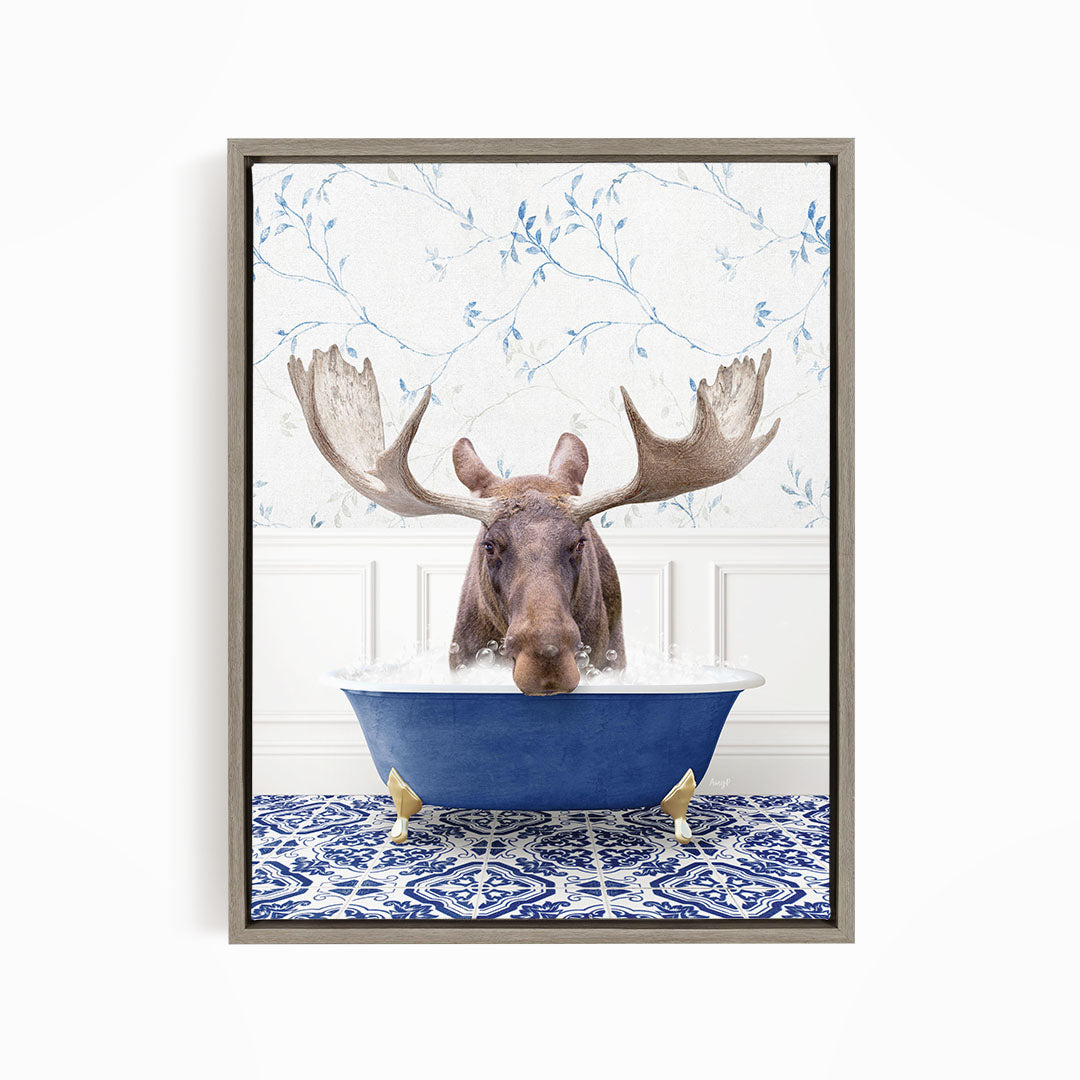 A moose with large antlers is sitting in a blue bathtub, surrounded by a patterned tile floor and a floral wallpaper background.