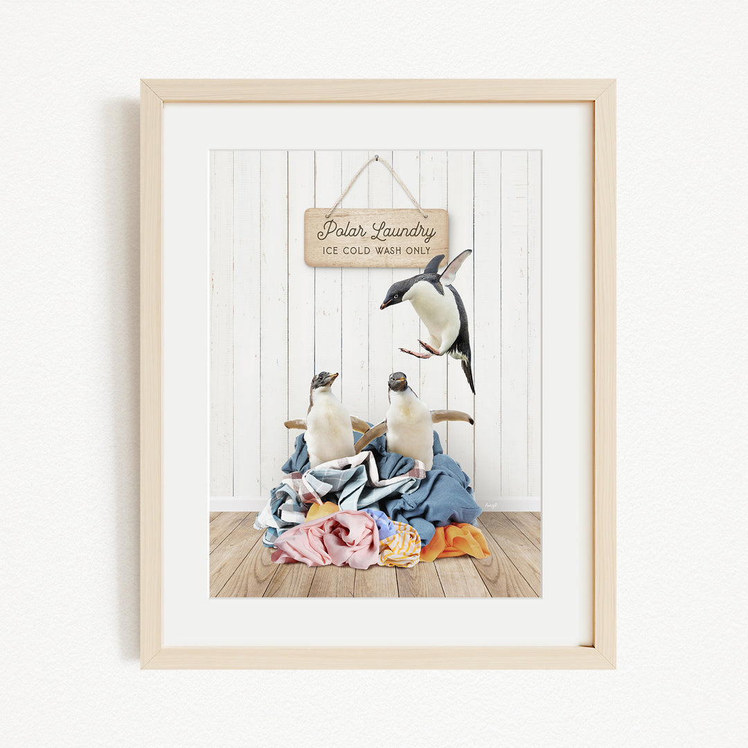 A framed photograph of two penguins sitting on a pile of clothes, with a sign that reads "Polar Laundry" above them.