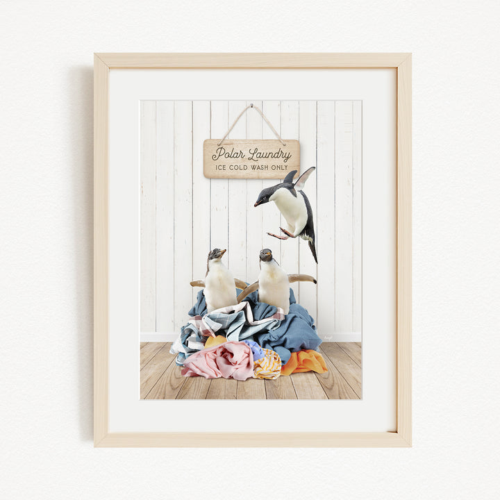 A framed photograph of two penguins sitting on a pile of clothes, with a sign that reads "Polar Laundry" above them.