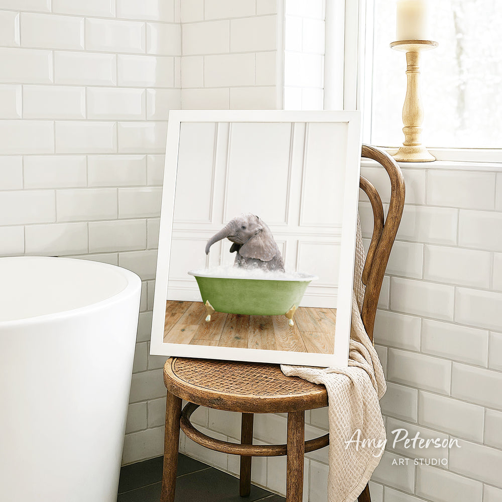 A framed image of a gray elephant sitting in a green bathtub, with a wooden chair and a white tiled wall in the background.