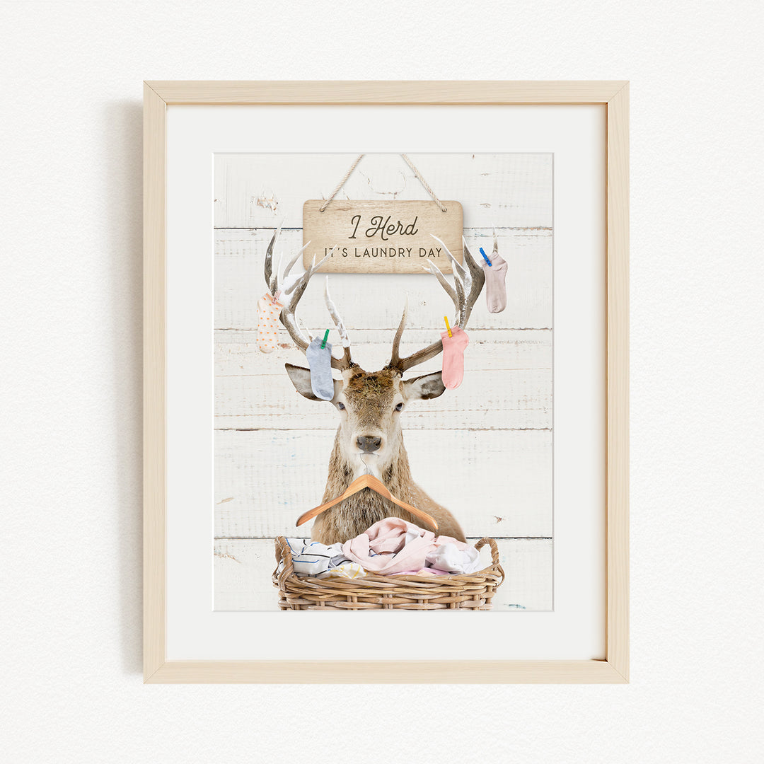 A framed image depicting a deer with antlers hanging from its head, holding a basket filled with clothes, and a sign above it that says "I hold it's laundry day".